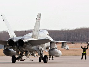 Military personnel guide a CF-18 Hornet into position at CFB Cold Lake in Alberta.