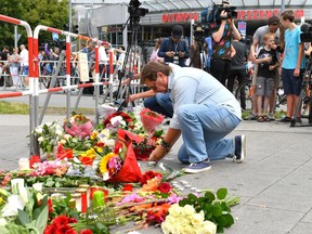 A man puts down flowers near a mall where a shooting took place leaving nine people dead the day before on Saturday, July 23, 2016 in Munich, Germany.