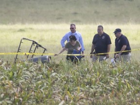 The partial frame of a hot air balloon is visible above a crop field as investigators comb the wreckage of a crash Saturday, July 30, 2016