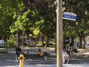 The corner of the John Innes Community Centre can be seen in the background and men lounge on the corner of Sherboure and Queen Street East on the edge of Moss Park in Toronto.