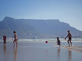 Visitors play in the surf near Table Mountain on Lagoon beach in Cape Town, South Africa, on Dec. 18, 2015.