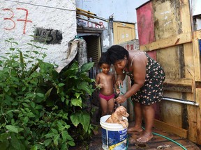 Jamilly Vitoria Santos da Silva, center, stands next to her mother, Rebeca Arruda as they wash a dog in a bucket in a favela as members of the Brazilian military along with health care workers to talk to residents about the threat of Zika virus.