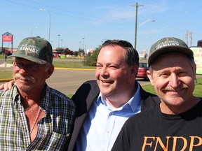 Jason Kenney poses with two new recipients of "Unite Alberta" caps in Stettler, Alta. The back of the FNDP shirt reads "Fund New Dance Projects."