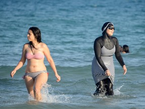 A woman wears a bikini next to burkini-clad swimmer