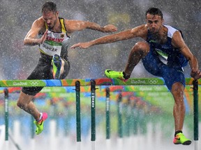 Matthias Buhler (left) of Germany and Milan Trajkovic (right) of Cyprus compete in the rain during the Men's 110m Hurdles qualifying round at the Olympic Stadium in Rio de Janeiro, Brazil, on Monday, Aug. 15, 2016.