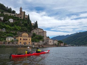 Kayakers take photos of the Church of Santa Maria del Sasso,the 15th-century structure standing tall on its precarious hillside perch, as they approach the village of Morcote, Italy.