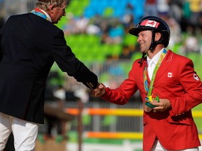 Gold medalist Britain's Nick Skelton, left, shakes hands with bronze medalist Canada's Eric Lamaze during a medal ceremony