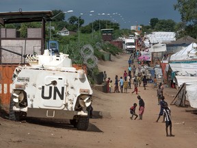 In this July 25, 2016 file photo, some of the more than 30,000 civilians sheltering in a United Nations base in South Sudan's capital Juba for fear of targeted killings by government forces walk by an armoured vehicle and a watchtower manned by Chinese UN peacekeepers. According to reports from victims which have come to light Monday Aug. 15, 2016, South Sudanese troops, fresh from winning a battle against opposition forces in the capital, Juba, on July 11, 2016,  went on a nearly four-hour rampage through a residential compound popular with foreigners, and the UN peacekeeping force stationed nearby are accused of refusing to respond to desperate calls for help.