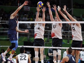 United States' Taylor Sander, left, spikes the ball as Canada's John Gordon Perrin (2), Graham Vigrass (17), and Gavin Schmitt block during a men's preliminary volleyball match at the 2016 Summer Olympics. (AP Photo/Jeff Roberson)
