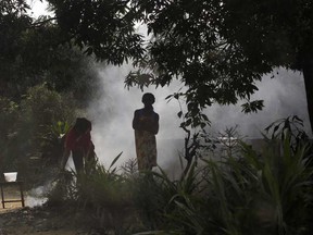 Residents of the Kisenso district of Kinshasa, Congo, stand by a smoking fire on Wednesday, July 20, 2016. There is much uncertainty about the control of yellow fever in Congo, where a surge of cases could spark further waves of the epidemic.