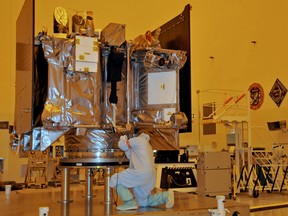 The OSIRIS-REx spacecraft sits on its workstand August 20, 2016 while an engineer checks the protective covering in a servicing building atKennedy Space Center, Florida.