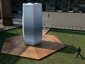 Dutch artist Daan Roosegaarde, right, walks past his Smog Free Tower on display at D-751art district in Beijing, Thursday, Sept. 29, 2016. In a city where smog routinely blankets the streets and chokes off clean air, a Dutch artist has offered an eccentric solution: a 20-foot metal tower that takes in smog and purifies it like a giant outdoor vacuum cleaner.