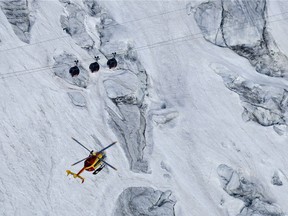 An EC-135 helicopter operated by the French Societe' Civile hovers, Friday, Sept. 9, 2016, near three cars of the Panoramic Mont Blanc cable car that stalled on Thursday after the cables tangled.
