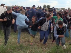 In this 2015 file photo taken from TV, a Hungarian camerawoman, center left in blue, kicks out at a young migrant who had just crossed the border from Serbia near Roszke Hungary