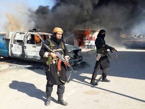 Two alleged ISIL fighters standing next to burning cars, at an undisclosed location in Iraq