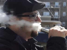 A man vapes outside a store selling electronic cigarettes and supplies.