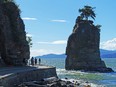 Stanley Park's iconic Siwash Rock thrusts from the ocean waters as sightseers travel the seawall pedestrian path, marvelling at mountain views.