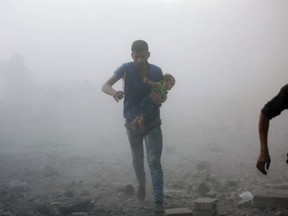 A Syrian man carrying a child emerges from a dust cloud following a reported airstrike on Kafr Batna, in the rebel-held Eastern Ghouta area, on the outskirts of the capital Damascus, on September 30, 2016.