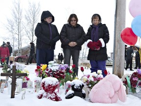 Residents of La Loche, Sask., say a prayer in front of a makeshift memorial at La Loche Community School on Sunday January 24, 2016.