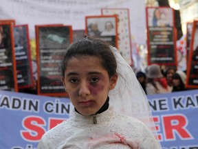 A Turkish girl, wearing a wedding dress and covered with fake bruises, stands in front of other protesters holding placard reading '' end violence'' during a demonstration to protest against rape, killings and domestic violence against women, in Ankara on November 27, 2011