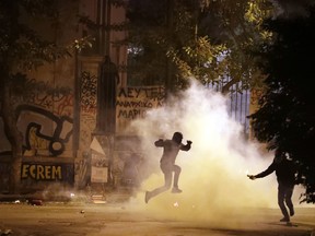 A protester jumps to avoid tear gas as another one prepares to throw a firebomb during a protest against the visit of US President Barack Obama in Athens, Tuesday, Nov. 15, 2016.