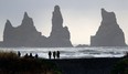 People walk on the black sand beach in Vik, Iceland.