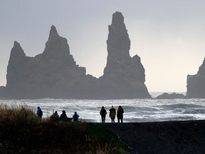 People walk on the black sand beach in Vik, Iceland.