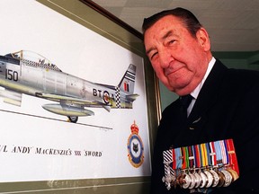 Andy MacKenzie wears his medals and stands beside a picture of his Sabre jet in 1997.