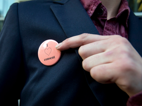 A victim of an alleged sexual assault -- who cannot be identified due to a publication ban -- points to her "I love consent" pin while leaving court in Calgary on Nov. 8, 2016.