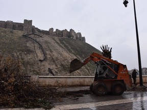 Municipal workers remove the dead branches of a tree near Aleppo's Citadel (background ) as the Syrian government starts to clean up areas formerly held by opposition forces in the northern city of Aleppo on Tuesday.