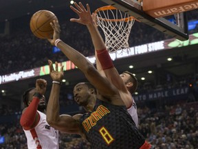 Atlanta Hawks centre Dwight Howard, centre, plays a pass under the basket despite pressure from Toronto Raptors centre Jonas Valanciunas, left, and DeMarre Carroll in Toronto on Friday.