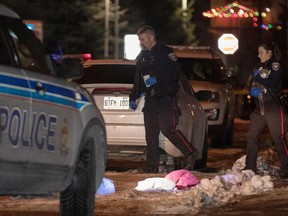 Ottawa Police officers, one carrying a cat, walks past the scene where a shooting victim was treated for his injuries and given CPR on McLeod Street in Ottawa on Sat., December 10.