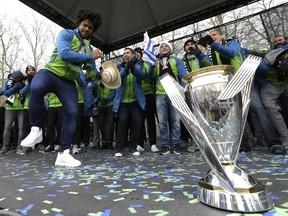 Seattle Sounders defender Roman Torres, left, dances on stage for teammates next to the MLS Cup trophy during a fan rally, Tuesday, Dec. 13, 2016, in Seattle. The Sounders defeated Toronto FC on Dec. 10, 2016 to win the MLS soccer championship. (AP Photo/Ted S. Warren)