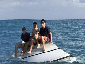 Teenagers Zack Sowder, left, Jacob Sowder and Brent Shishido, right, of Orange County, Calif., sit on an capsized vessel offshore of Little Torch Key in the Florida Keys on Tuesday.