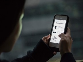 This photo illustration taken on January 5, 2017 in Beijing shows a user posing with an iPhone showing an installed New York Times app on the device.  Apple has removed the New York Times from its China app store, the tech giant said, after authorities told the company the app breached regulations.