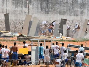 Prisoners cover themselves using makeshift shields as riot police agents (out of frame) fire rubber bullets during a rebellion at the Alcacuz Penitentiary Center near Natal in Rio Grande do Norte, Brazil on January 17.  A deadly tumult exploded on Saturday at Natal's overcrowded jail, on Sunday, police had invaded the prison and ended a night riot and found 26 prisoners dead.
