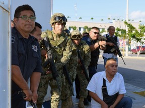 Policemen and soldiers take cover at the place where a shooting erupted ensuing an attack against the building of the Quintana Roo State Prosecution