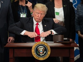 US President Donald Trump takes the cap off a pen to sign an executive order to start the Mexico border wall project at the Department of Homeland Security facility in Washington, DC, on January 25, 2017.