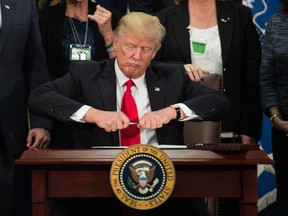 U.S. President Donald Trump takes the cap off a pen to sign an executive order to start the Mexico border wall project at the Department of Homeland Security facility in Washington, DC, on January 25, 2017.