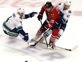 Chicago Blackhawks centre Jonathan Toews, centre, battles for the puck between Vancouver Canucks right wing Alexandre Burrows, left, and left wing Sven Baertschi during the third period Sunday in Chicago. The Blackhawks won 4-2.