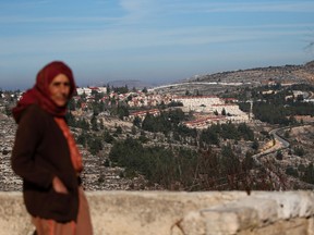 A Palestinian woman stands in the West Bank village of Lubban ash-Sharkiya, in front of a view of the Jewish settlement of Eli.