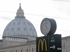 A sign showing the direction of a McDonald's restaurant is seen with the cupola of St. Peter's Basilica in the background, on January 3, 2017 in Rome.