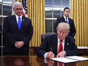Donald Trump signs an executive order as Vice President Mike Pence looks on at the White House in Washington, DC on January 20, 2017