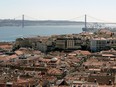 The rooftops of city apartments sit beside the Tagus river near the 25th April Tagus Bridge in Lisbon, Portgual.