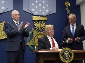 President Donald Trump, center, grabs the hand of Defense Secretary James Mattis, right, after he signed an executive action on rebuilding the military during an event at the Pentagon in Washington, Friday, Jan. 27, 2017. Vice President Mike Pence watches, left.