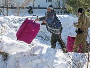 A Somali man tosses his family's luggage over the the U.S.-Canada border in front of a U.S. Border Patrol agent near Hemmingford, Que., on Friday, February 17, 2017.