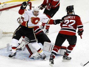 Calgary Flames' Matt Stajan gets all tangled up with New Jersey Devils' goaltender Cory Schneider after scoring a goal during NHL action Friday night at the Meadowlands, N.J. Kyle Quincey of the Devils arrives too late. The Flames made it three straight wins with a 4-3 victory in overtime.