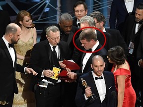 La La Land producer Fred Berger (R) speaks at the microphone as production staff and Brian Cullinan scramble over the presentation error