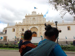 Two indigenous women stroll through the central plaza of Antigua Guatemala, Guatemala, with the San Jose cathedral behind them.