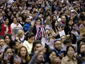 In this Wednesday, Feb. 15, 2017, file photo, people wave U.S. flags during a naturalization ceremony at the Los Angeles Convention Centre